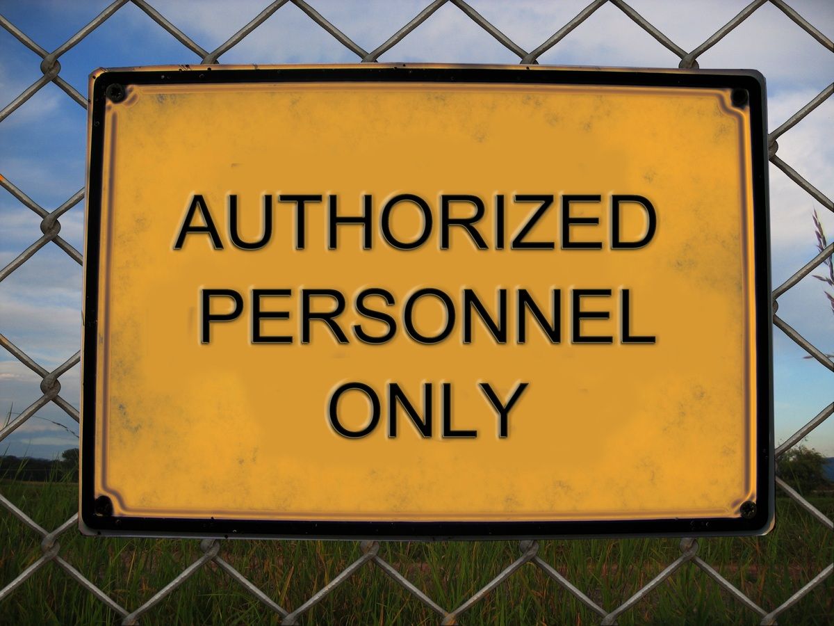 Yellow sign on a chain-link fence reads AUTHORIZED PERSONNEL ONLY with a blue sky and green grass in the background.