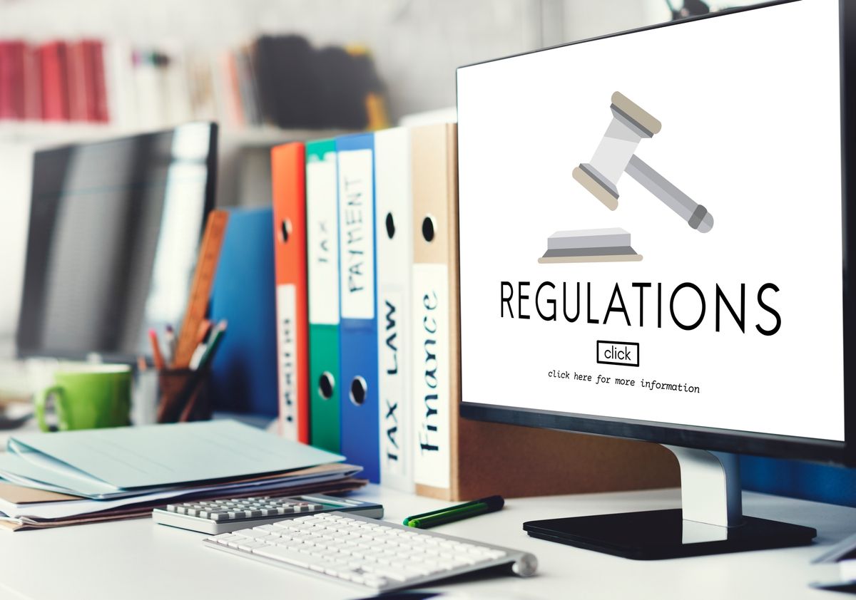 Monitor shows REGULATIONS text and gavel icon; desk has folders labeled TAX LAW, FINANCE, PAYMENT.