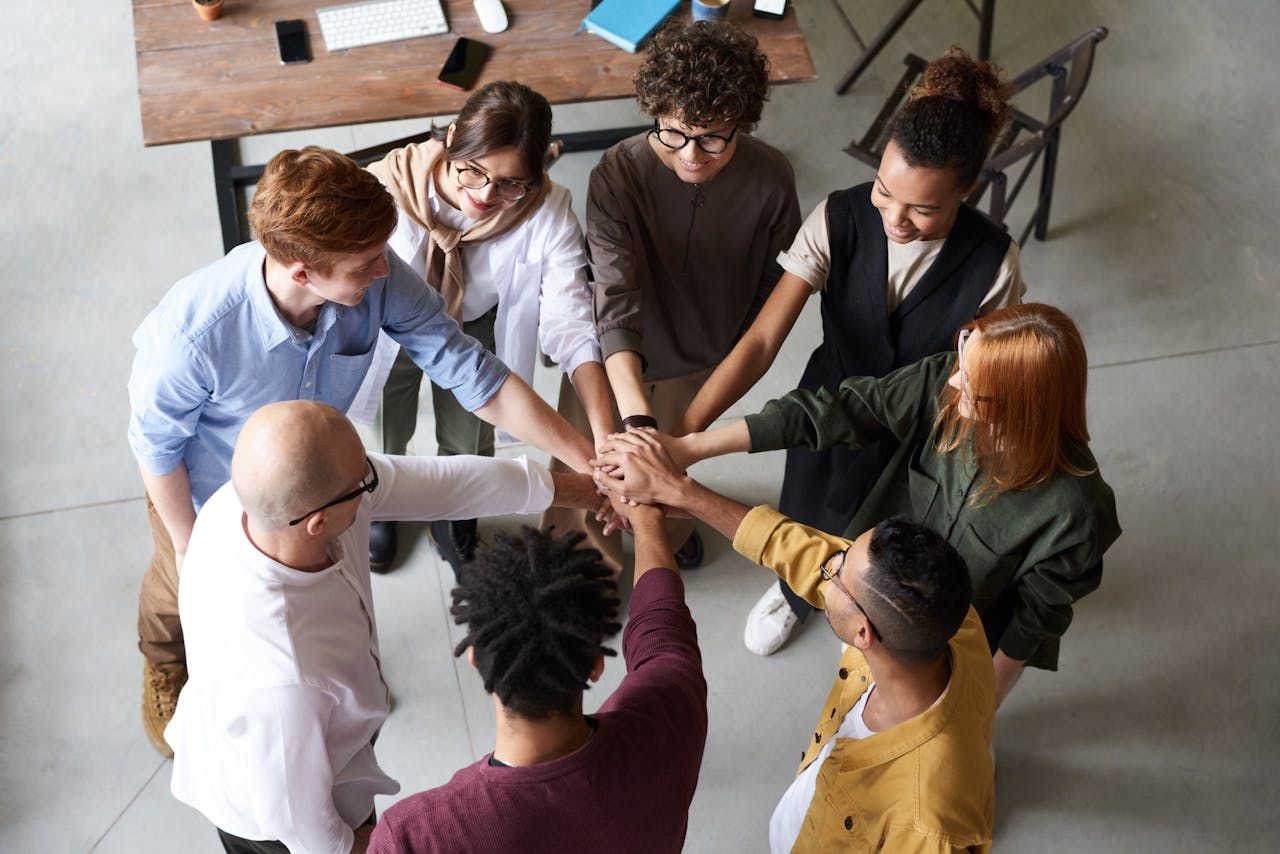 Diverse group of six business professionals standing in a circle, stacking their hands in the middle.