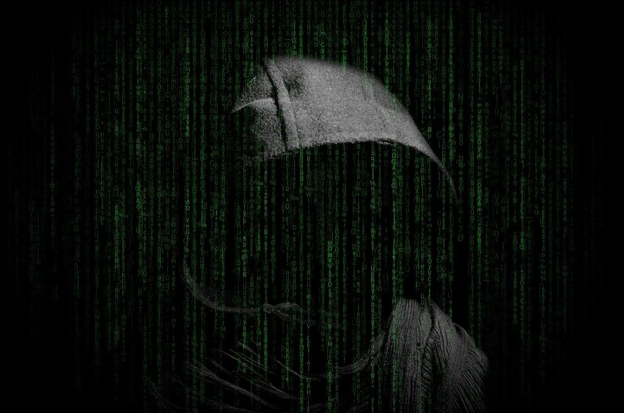 Hooded figure obscured by falling green digital code on a dark background.